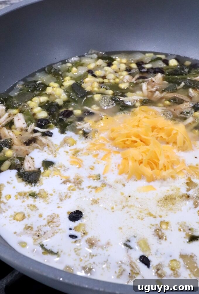 Heavy cream and shredded cheddar cheese being stirred into a large pot of Chicken Poblano Soup, making it rich and creamy.
