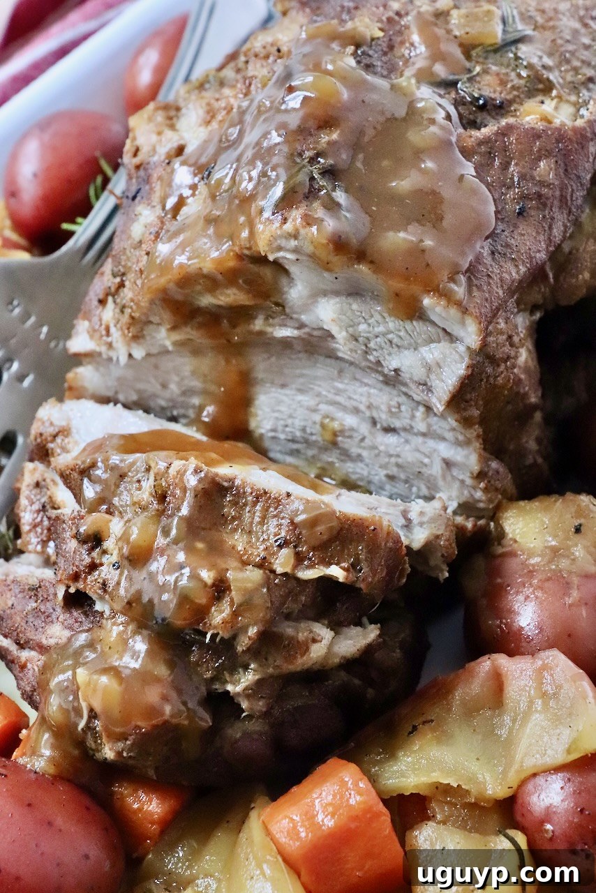 cooked pork roast, partially sliced on a large platter with roasted vegetables and gravy drizzled on top