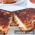 A delicious Pizza Grilled Cheese sandwich cut in half, revealing its cheesy interior, on a plate.