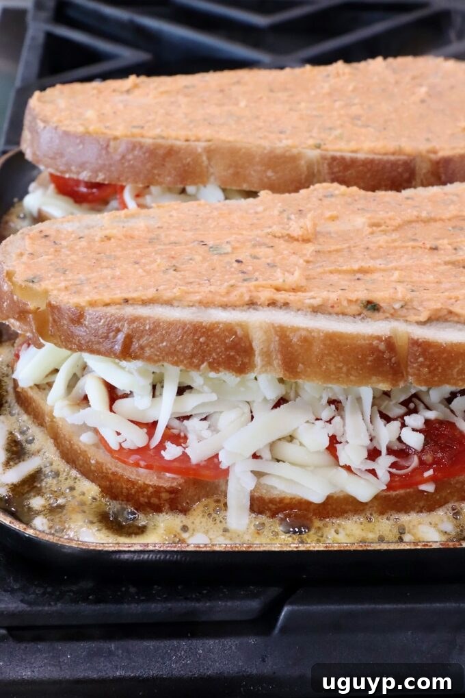 Several assembled Pizza Grilled Cheese sandwiches sizzling in a large skillet, their crusts beginning to crisp and turn golden brown as the cheese melts inside.