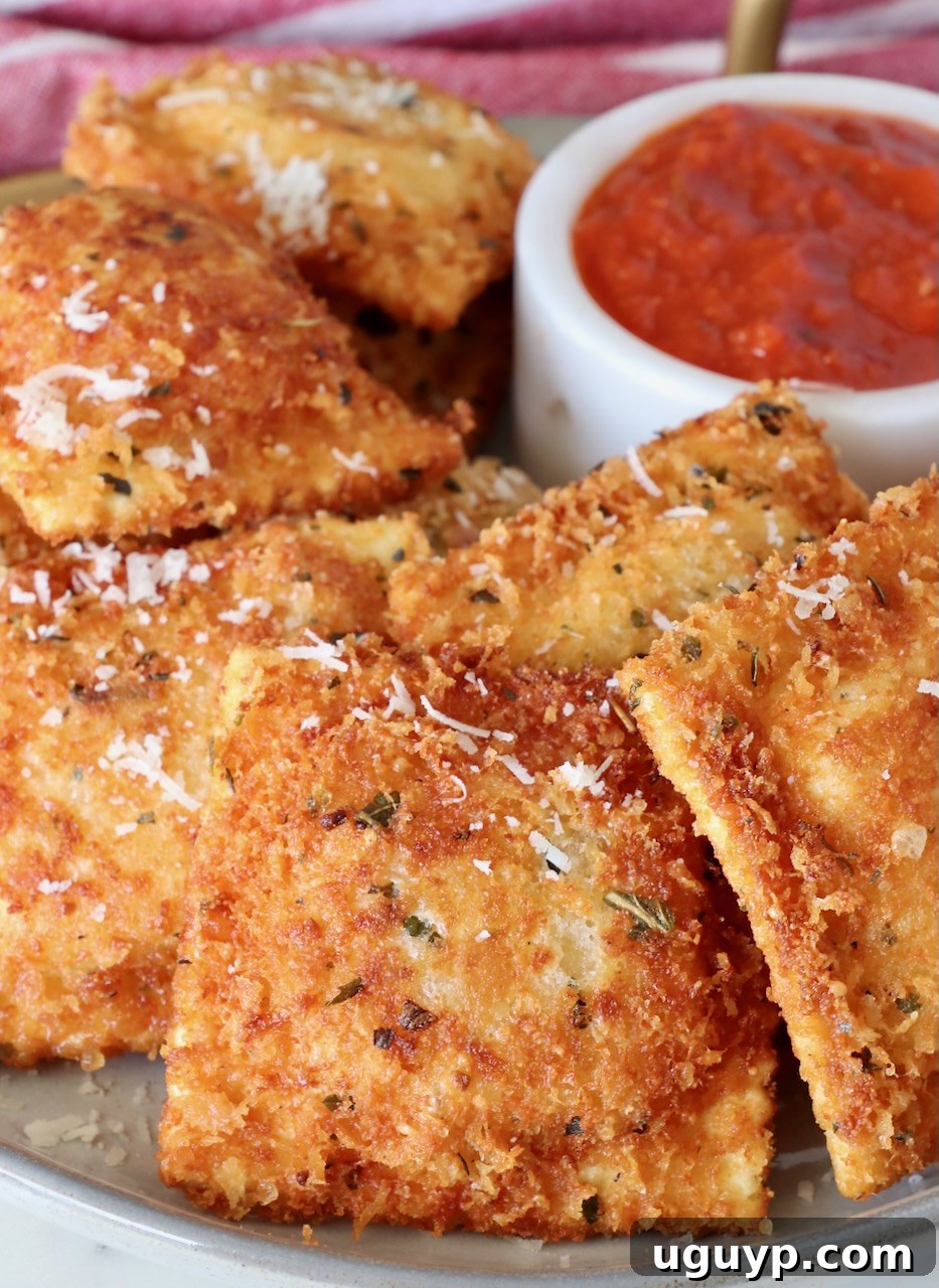 Crispy golden brown toasted ravioli stacked high on a plate, with a bowl of rich marinara sauce in the background, ready for dipping.