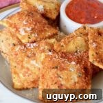 A mouthwatering photo of toasted ravioli stacked on a plate, with a small bowl of marinara sauce for dipping.