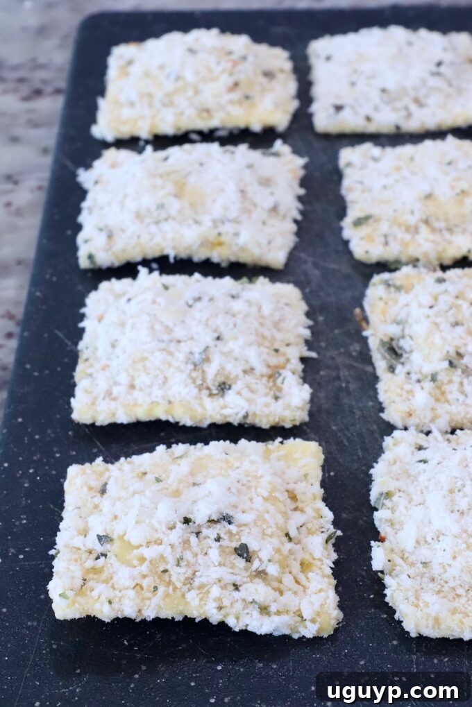 Frozen ravioli uniformly coated in a golden breadcrumb mixture, neatly arranged on a cutting board, ready for cooking.