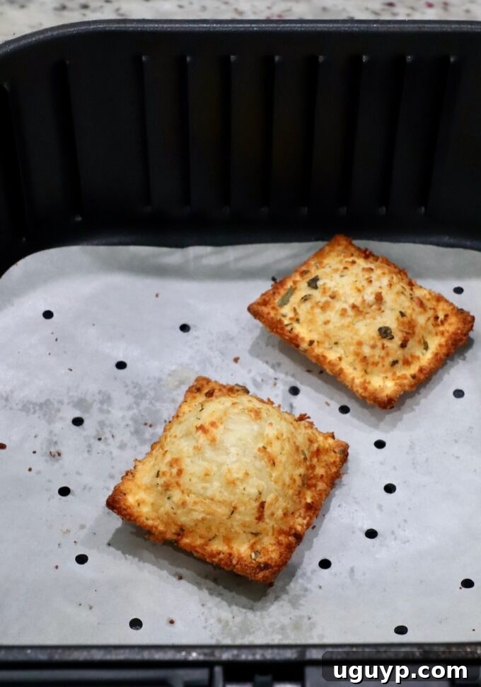Two perfectly toasted raviolis nestled in an air fryer basket lined with parchment paper, highlighting the air frying method.