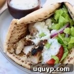 pita bread filled with chicken gyros meat, tzatziki sauce, shredded lettuce, sliced onions and tomatoes, on a plate