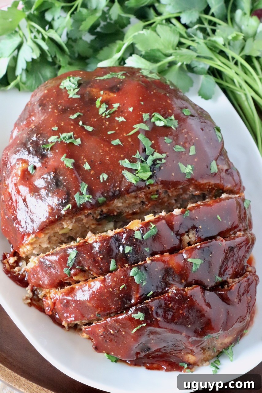 glazed, cooked meatloaf, partially sliced on a plate with fresh parsley