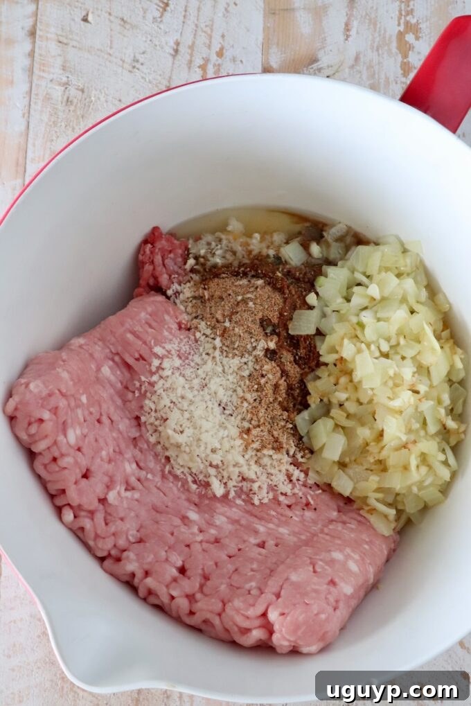 raw ground beef and ground pork in a large mixing bowl with breadcrumbs, cooked onions, and spices