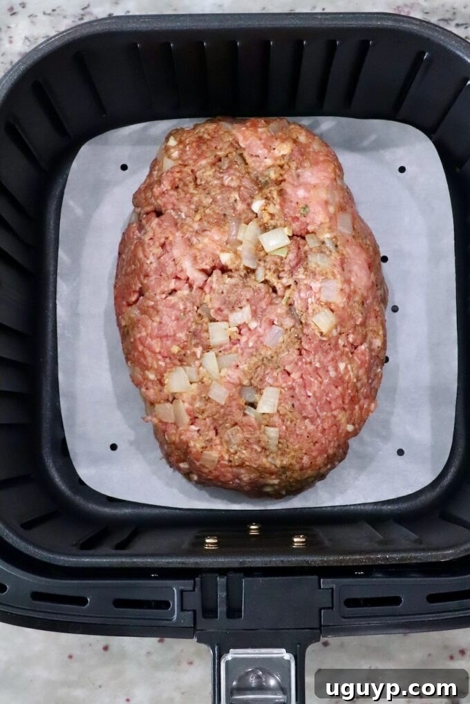 uncooked meatloaf in an air fryer basket with a parchment paper liner