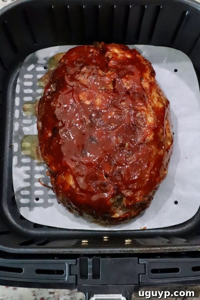 cooked, glazed meatloaf in an air fryer basket with a parchment paper liner