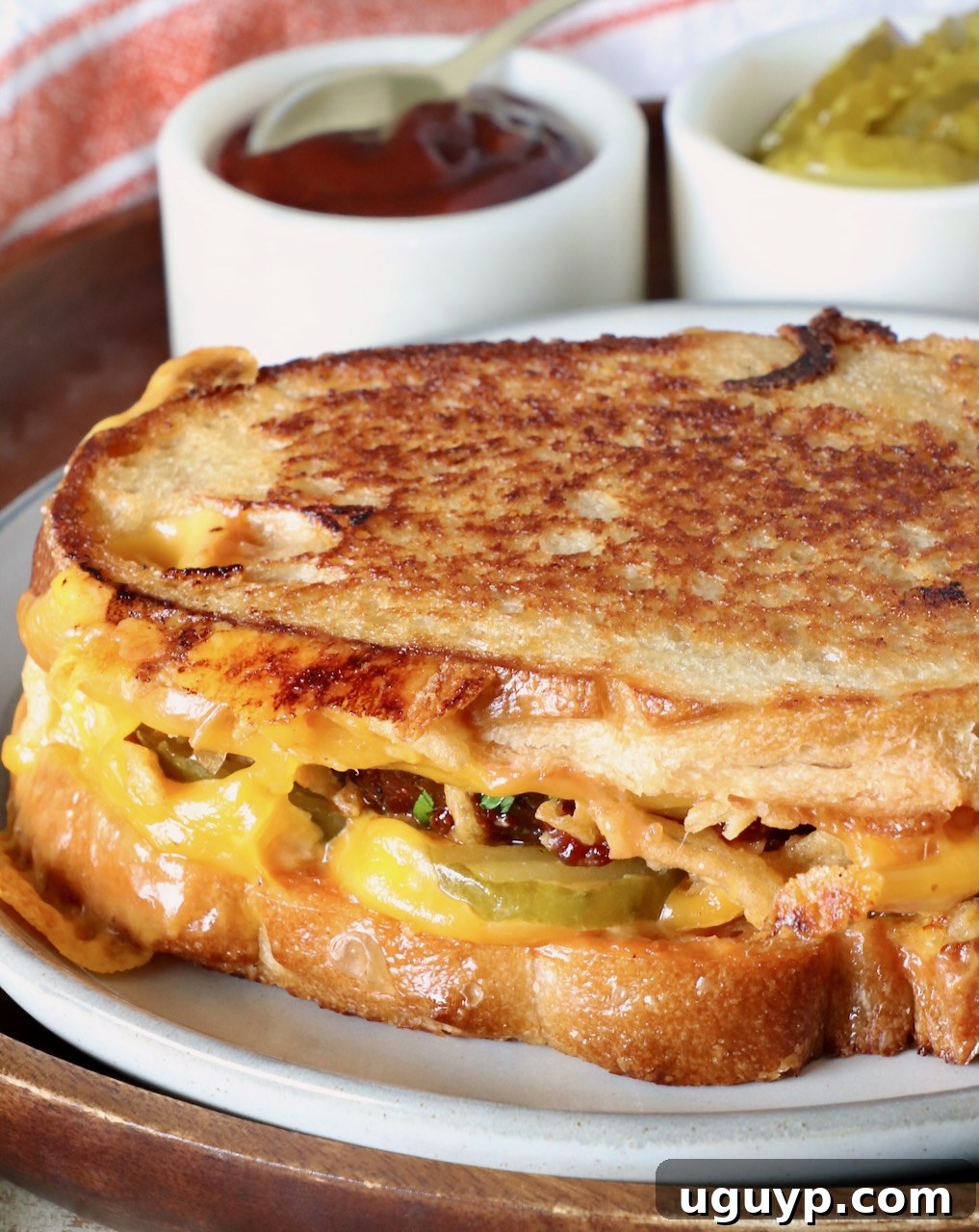 A perfectly assembled meatloaf sandwich on a plate, with a small bowl of BBQ sauce and pickles in the background.