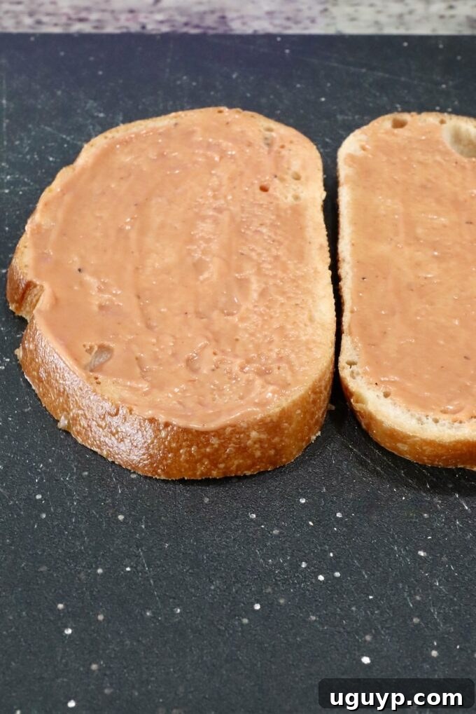 A cutting board with two slices of bread, each spread with a mixture of BBQ sauce and mayonnaise.
