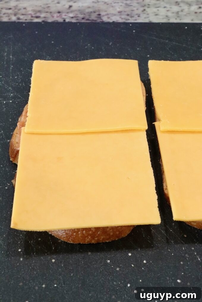 Two slices of bread on a cutting board, each topped with slices of sharp cheddar cheese.