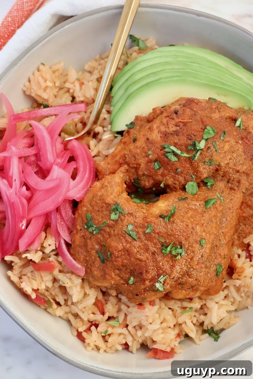 Adobo chicken on top of Mexican rice in a bowl with sliced avocado and pickled onions, ready to be enjoyed.