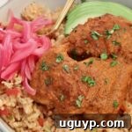 Cooked chicken covered in adobo sauce on top of rice in a bowl with avocado and pickled onions, an inviting dish.