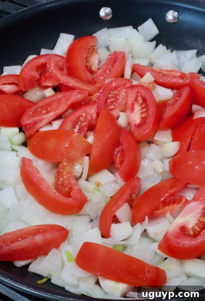Diced onions and sliced tomatoes sautéing in a skillet, the first step in making the adobo sauce.