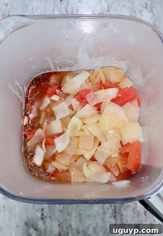 Cooked onions and tomatoes transferred to a blender with other adobo sauce ingredients, ready for pureeing.