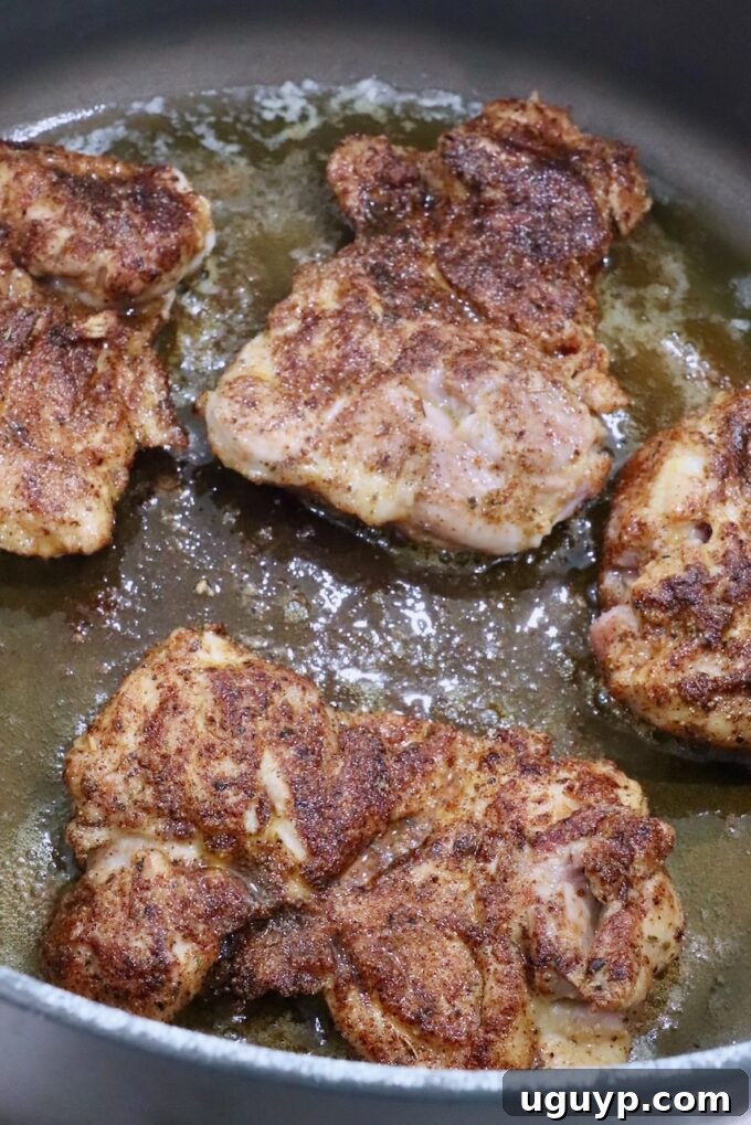 Seasoned chicken thighs searing in a large Dutch oven with butter and avocado oil, developing a golden crust.