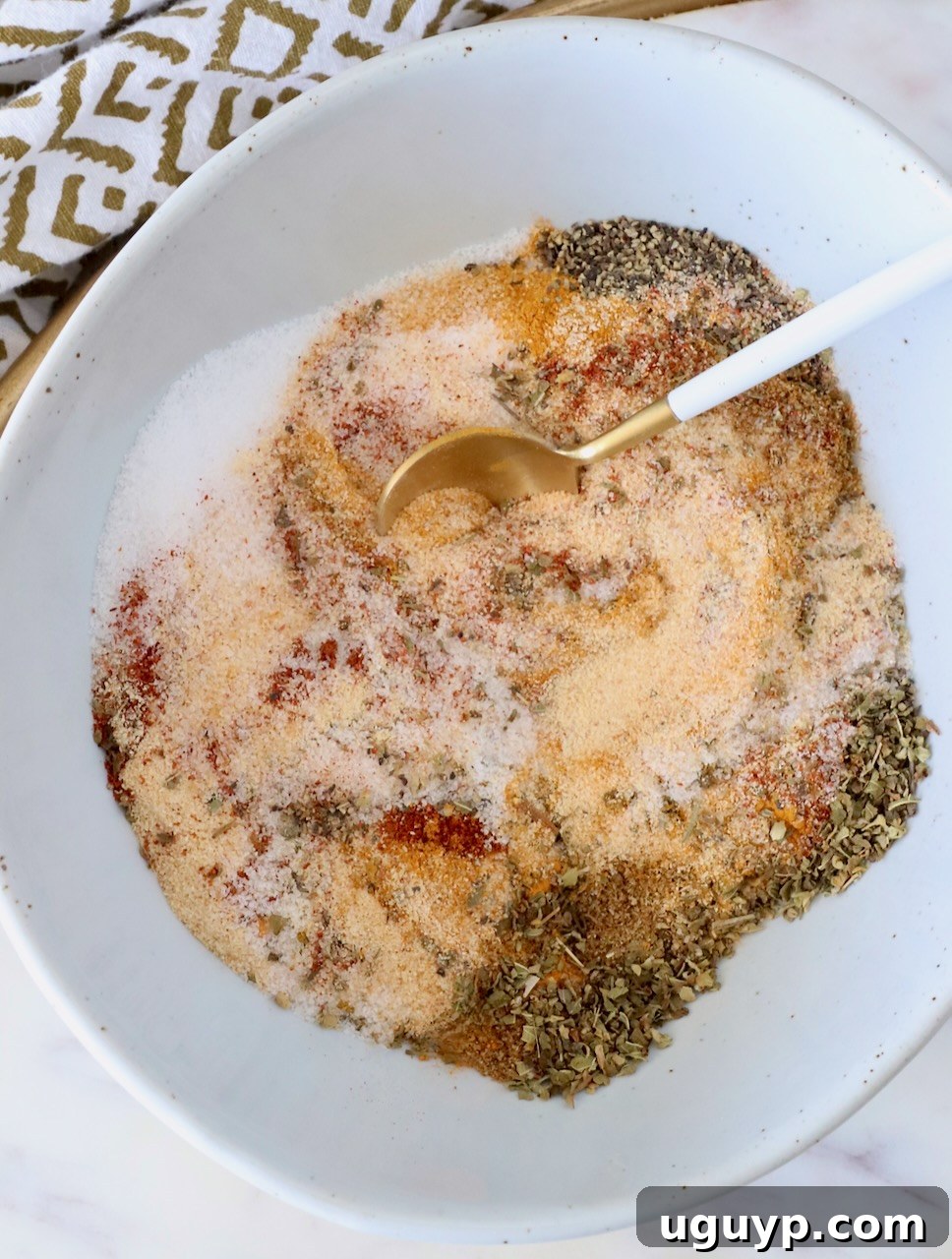 various dried herbs and spices mixed together in a bowl with a small spoon, showcasing a vibrant homemade Adobo seasoning blend