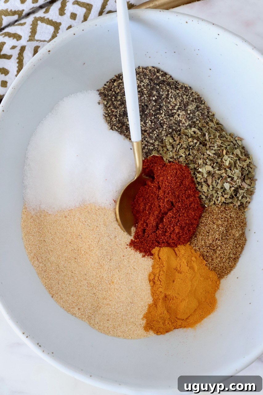 dried herbs and spices separated in a bowl with a spoon, highlighting the individual components of Adobo seasoning