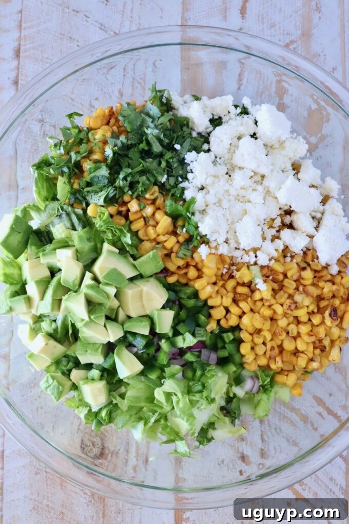 Freshly chopped corn, avocado, cotija cheese, cilantro, and lettuce in a large glass bowl