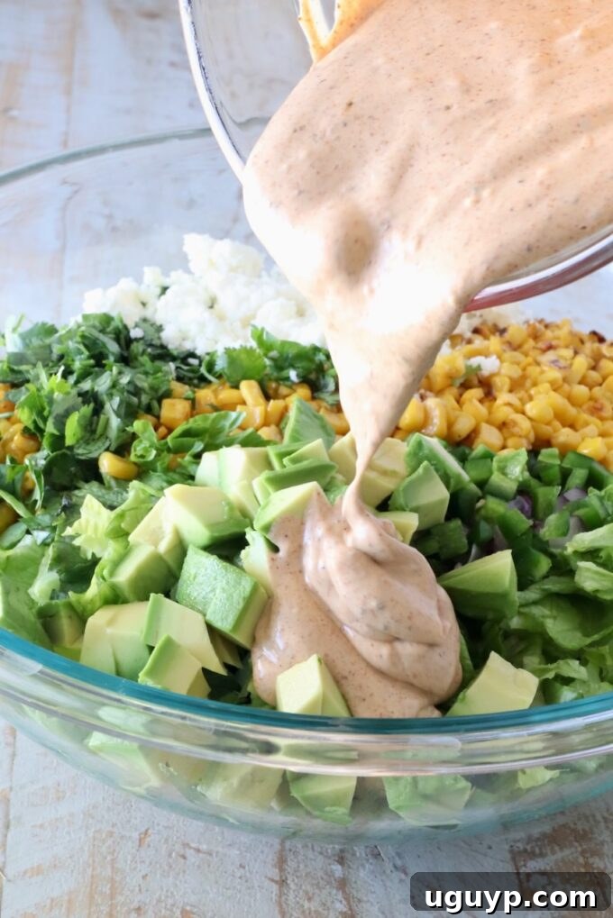 Pouring chili lime dressing over a bowl of fresh salad ingredients