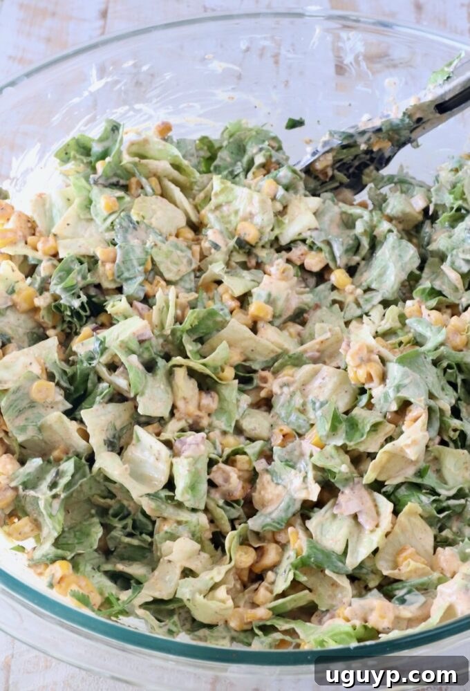 Mexican street corn salad being tossed in a large glass bowl with kitchen tongs