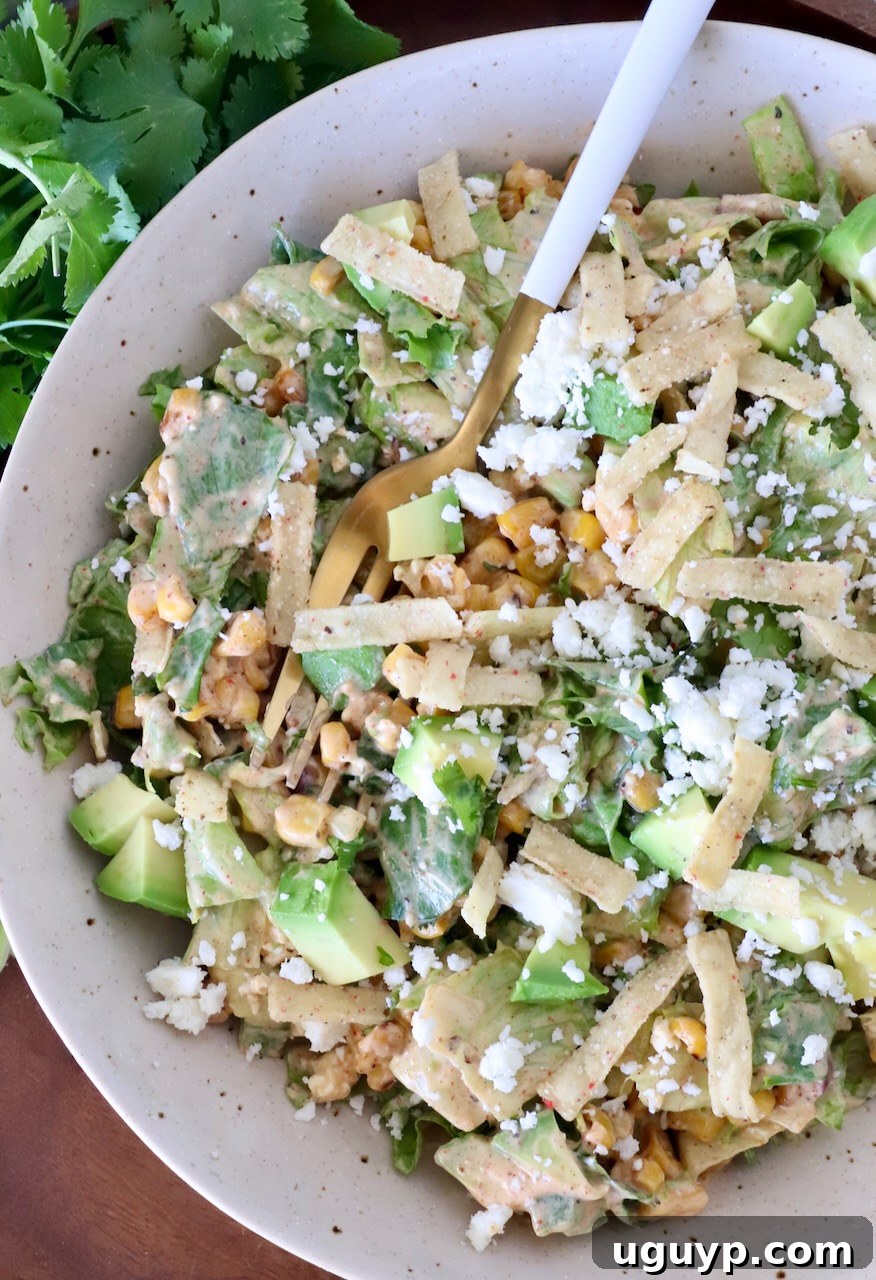Delicious Mexican street corn salad served in an individual bowl with a fork, garnished with tortilla strips