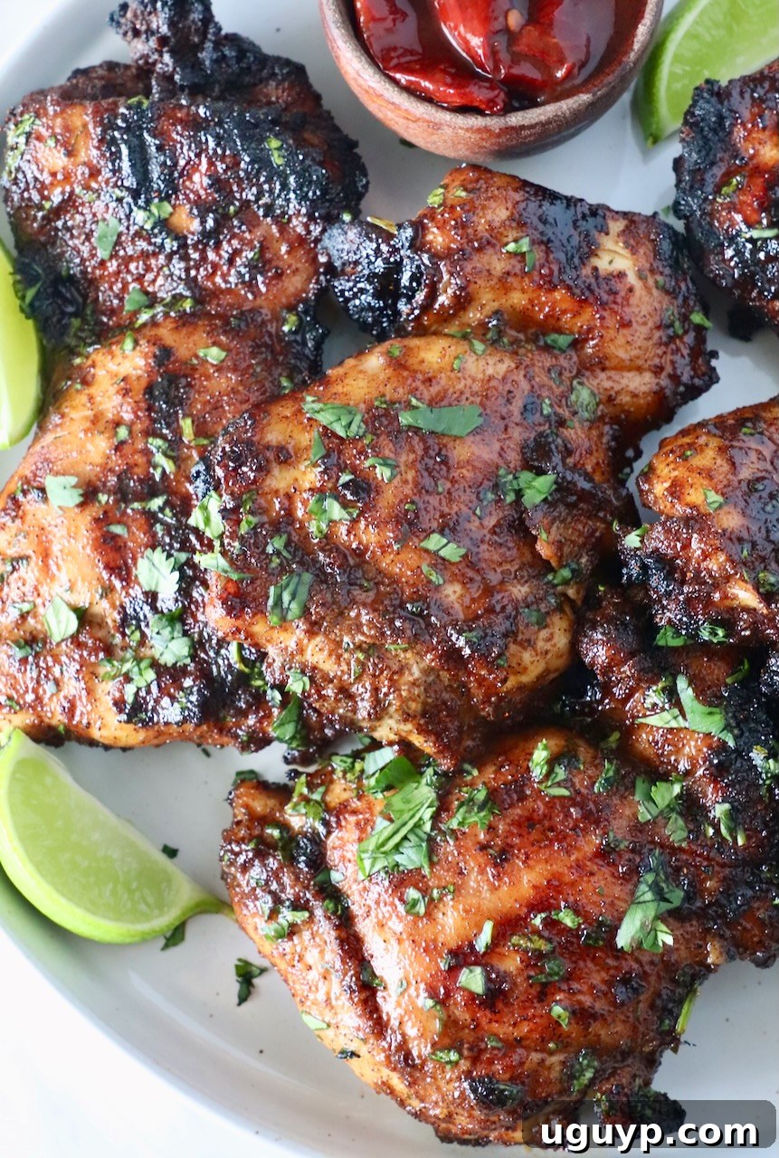 Glazed grilled chipotle honey chicken thighs stacked on a plate with fresh cilantro and lime wedges, showcasing its golden-brown char and sticky glaze.