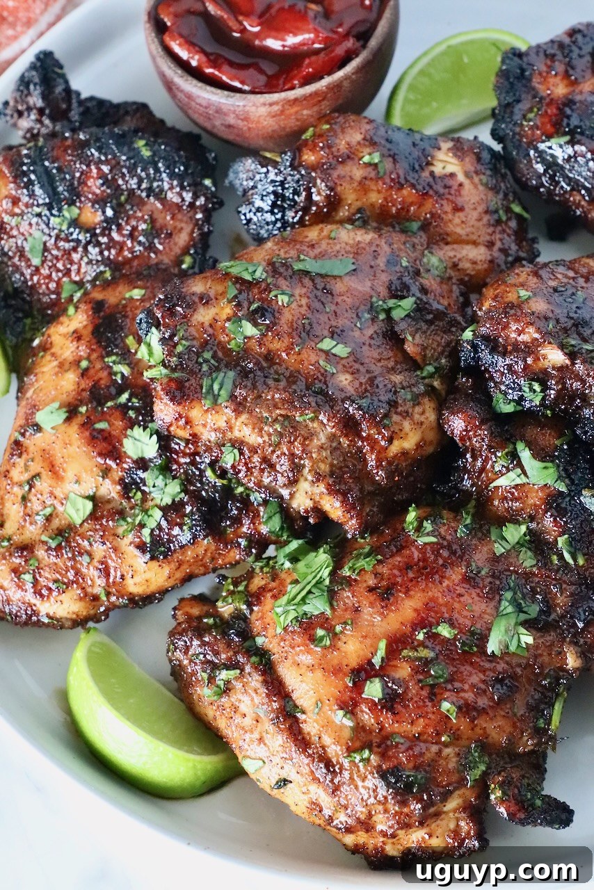 Grilled chicken thighs, perfectly stacked, with fresh lime wedges and small wooden bowl of chipotle peppers.
