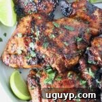 Grilled chicken thighs stacked up on a plate with fresh cilantro and lime wedges