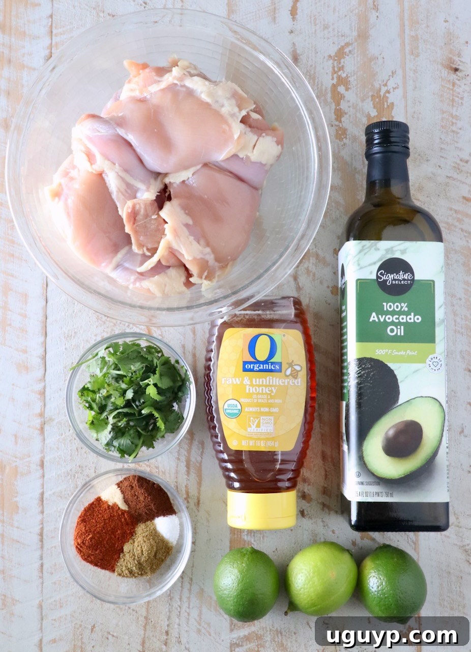 Raw ingredients for Chipotle Honey Chicken laid out on a wooden board, including chicken thighs, spices, honey, lime, and cilantro.
