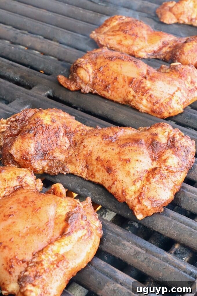 Seasoned raw chicken thighs laid out on a preheated outdoor grill, ready to cook and develop beautiful char marks.