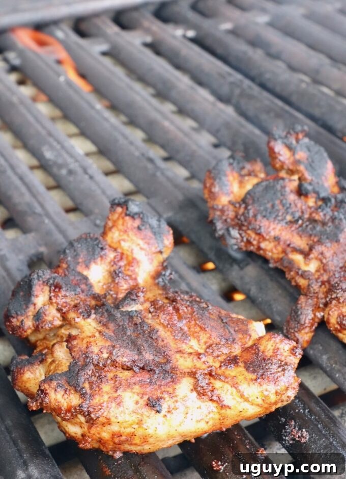 Grilled chicken thighs cooking on a hot grill, showing developing grill marks and a lightly browned surface.