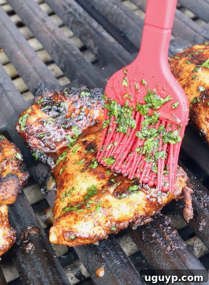A grilling brush applying the vibrant cilantro honey glaze onto a piece of grilled chicken thigh on the barbecue, creating a sticky, caramelized finish.