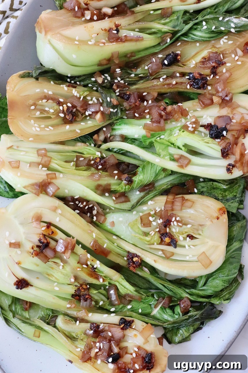 Cooked baby bok choy topped with a glossy garlic shallot soy sauce, beautifully arranged on a white plate, ready to serve.