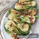 A close-up of cooked baby bok choy on a plate, generously coated in a flavorful garlic shallot soy sauce, highlighting its vibrant green leaves.