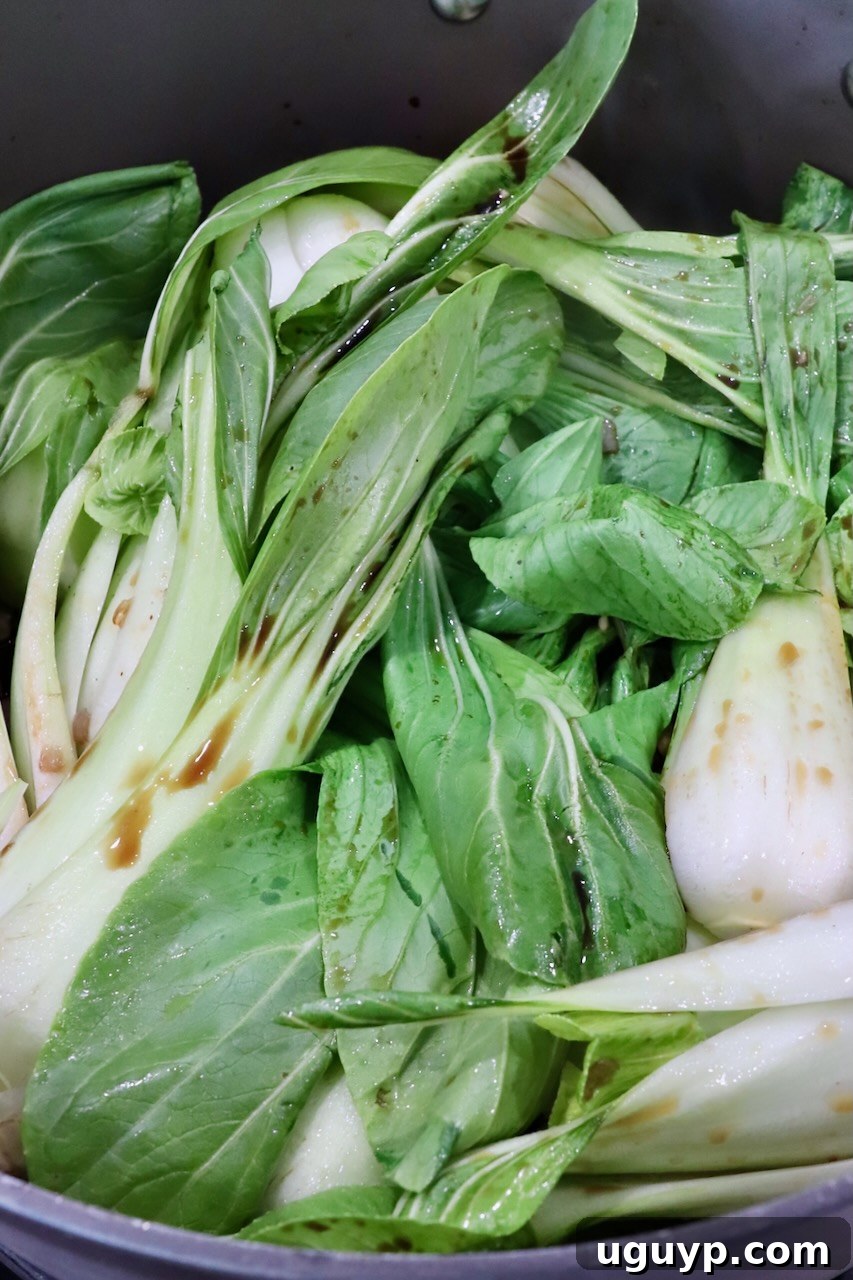 Baby bok choy cooking in a large, hot pot with aromatic garlic and shallots, coated in a savory sauce.