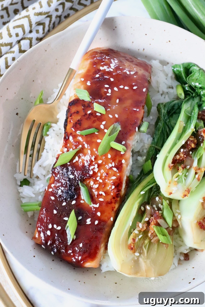 A delightful meal featuring a piece of perfectly cooked miso glazed salmon, fluffy white rice, and a vibrant serving of sautéed baby bok choy, all presented in a bowl.