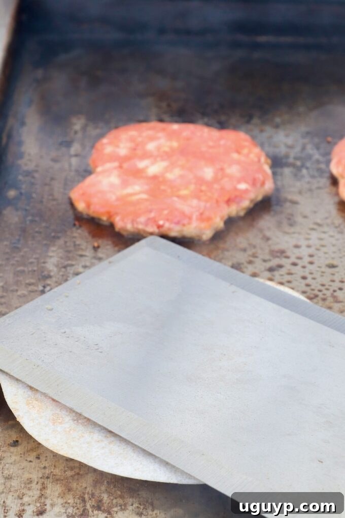 burger patty smashed with a large metal spatula on a griddle