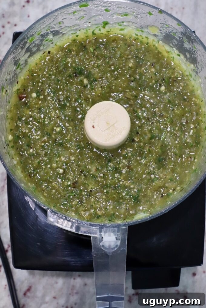 Blended salsa verde in a food processor, showing a vibrant green color and chunky texture.