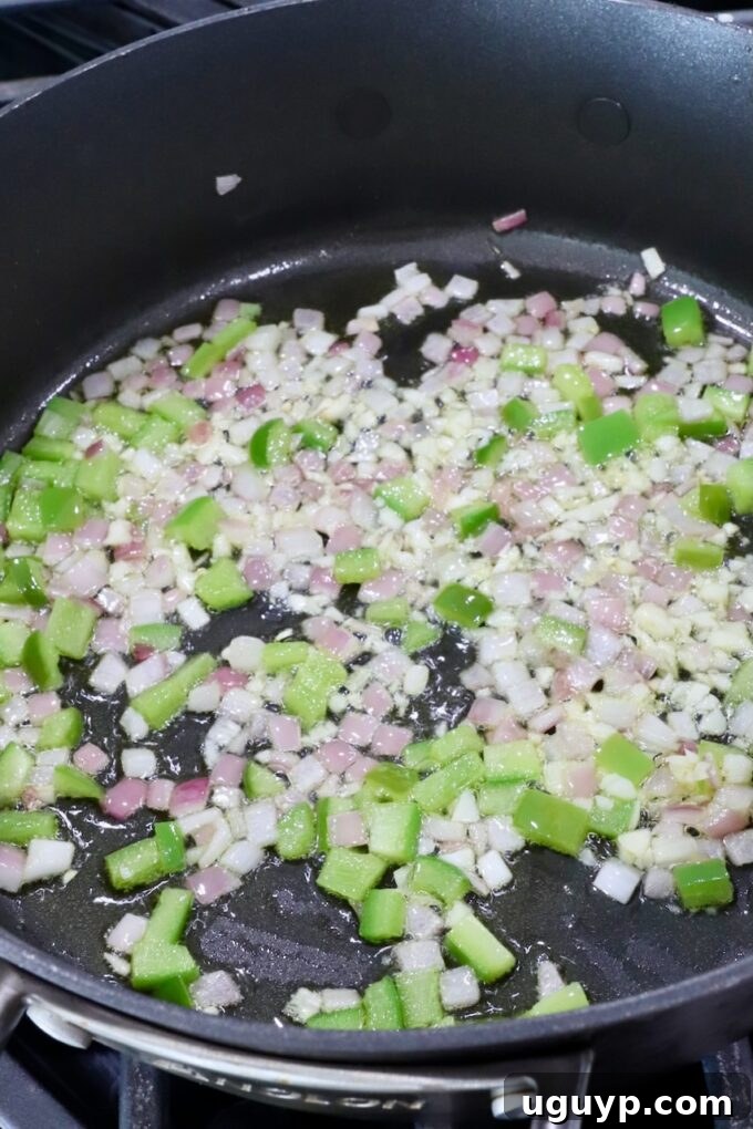 Minced red onion and green bell pepper sautéing in olive oil in a small skillet on the stove.