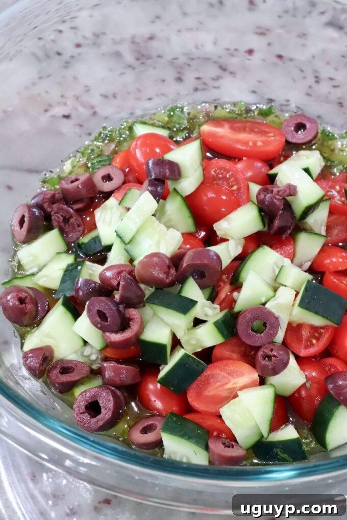 Diced cucumber, quartered cherry tomatoes, and sliced Kalamata olives in a large glass bowl, ready for the dressing.
