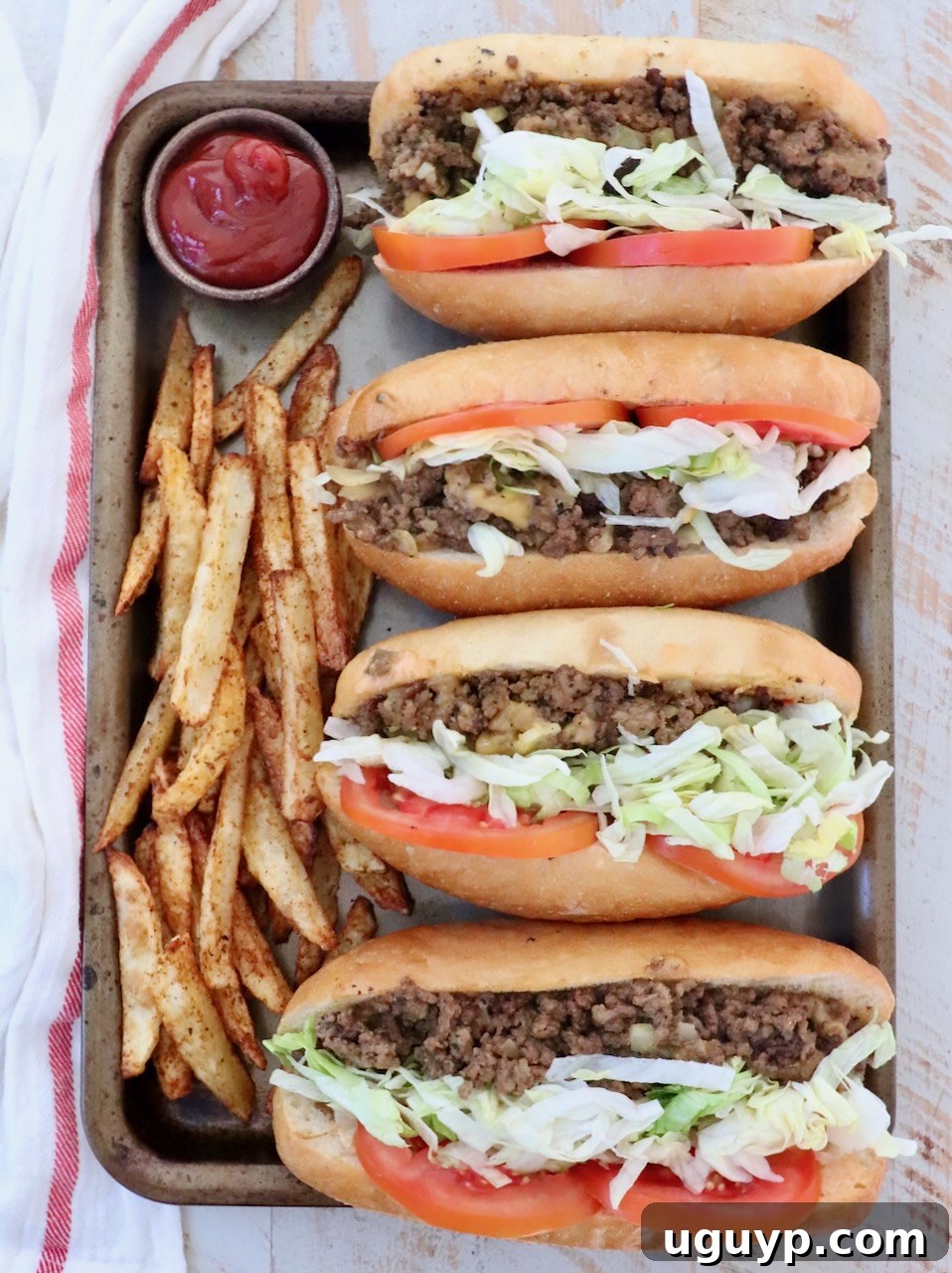 Four mouth-watering chopped cheese sandwiches on a baking sheet, surrounded by golden, crispy french fries and a small bowl of ketchup, ready to be devoured.