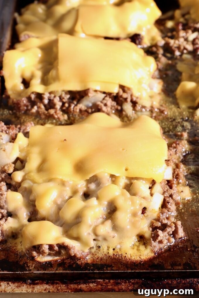 Melted slices of American cheese perfectly blanketing portions of seasoned ground beef on a griddle, moments before being chopped and mixed into the meat.