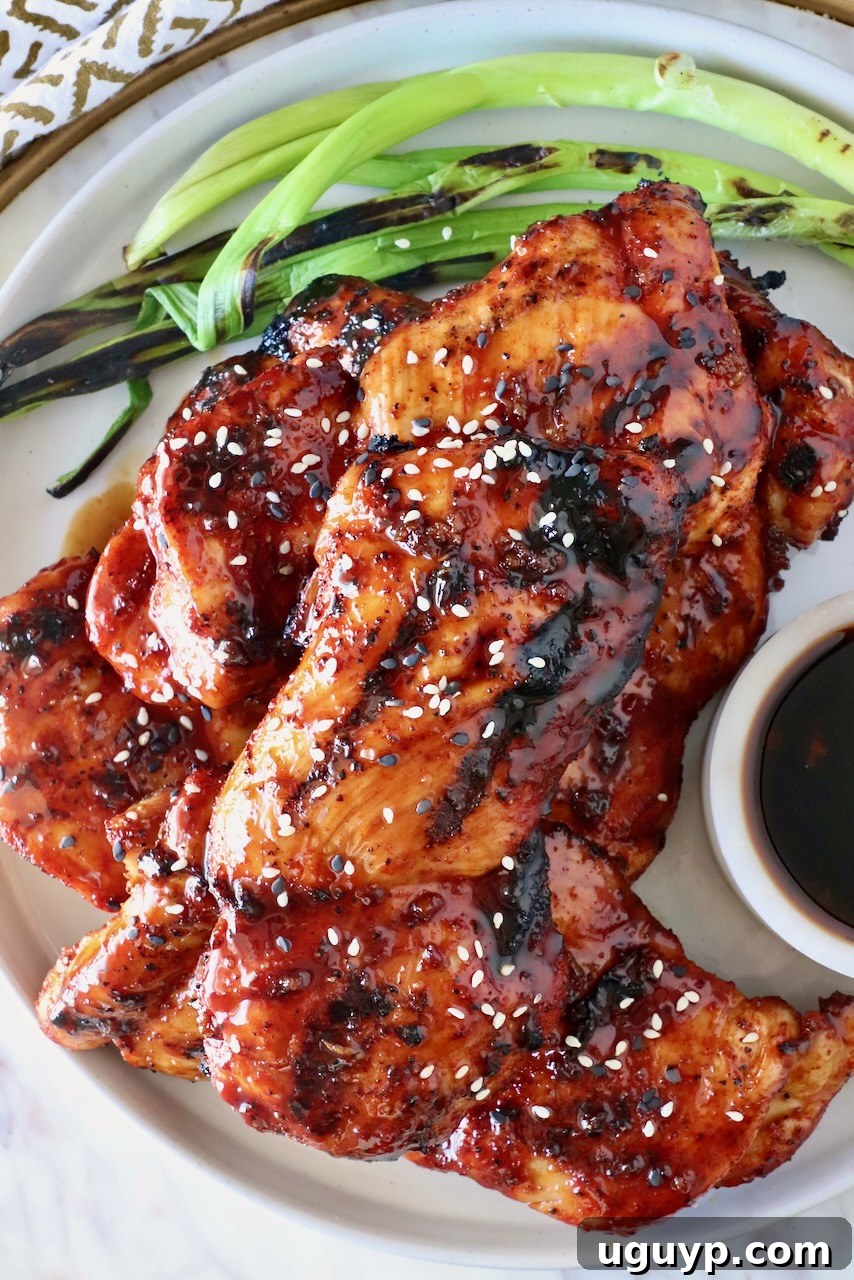 Glossy, grilled Korean BBQ chicken thighs stacked on a plate, garnished with fresh green onions.