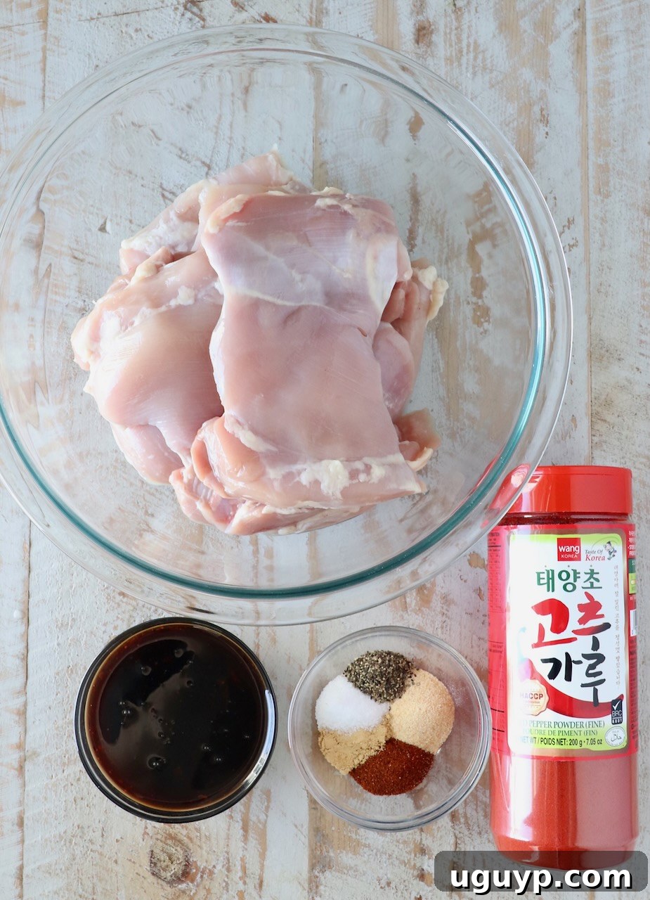 Individual bowls of various Korean BBQ chicken seasoning ingredients like gochugaru, smoked paprika, garlic powder, and ginger, arranged on a white wooden board.