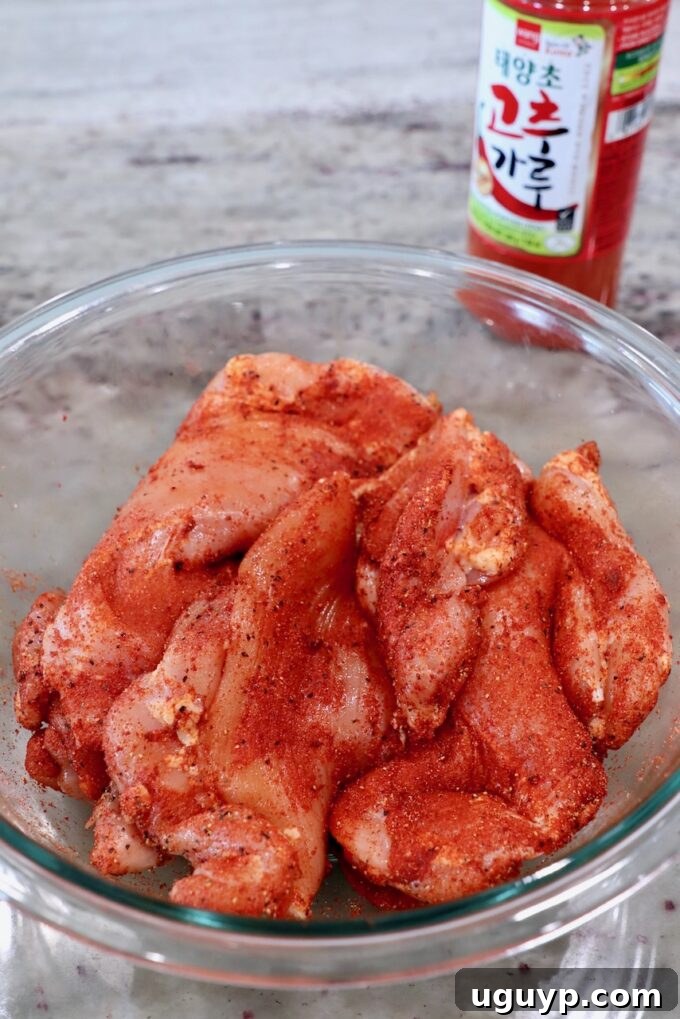Boneless, skinless chicken thighs generously coated in a vibrant homemade Korean BBQ dry rub, resting in a glass bowl.