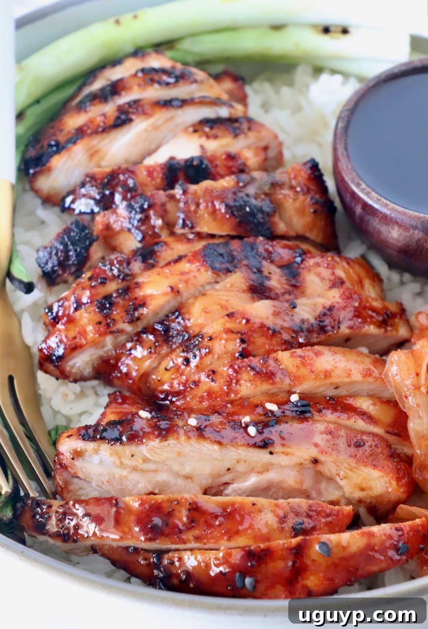 Sliced Korean BBQ chicken thighs served over white rice in a bowl, garnished with green onions and a side of Korean BBQ sauce.