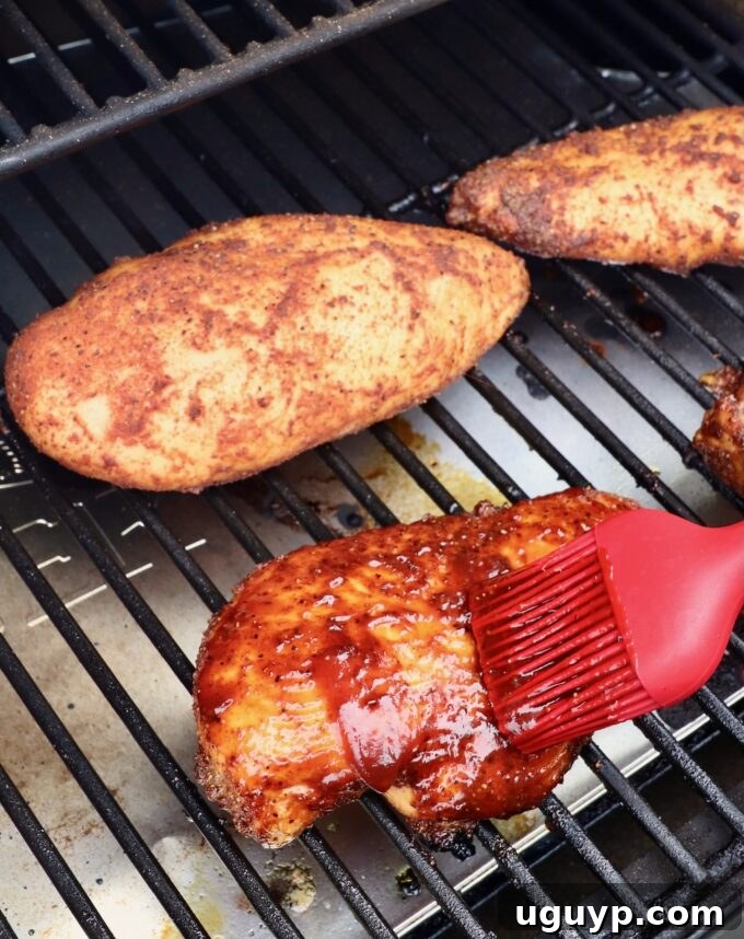 red brush with bbq sauce being brushed on a chicken breast on a smoker