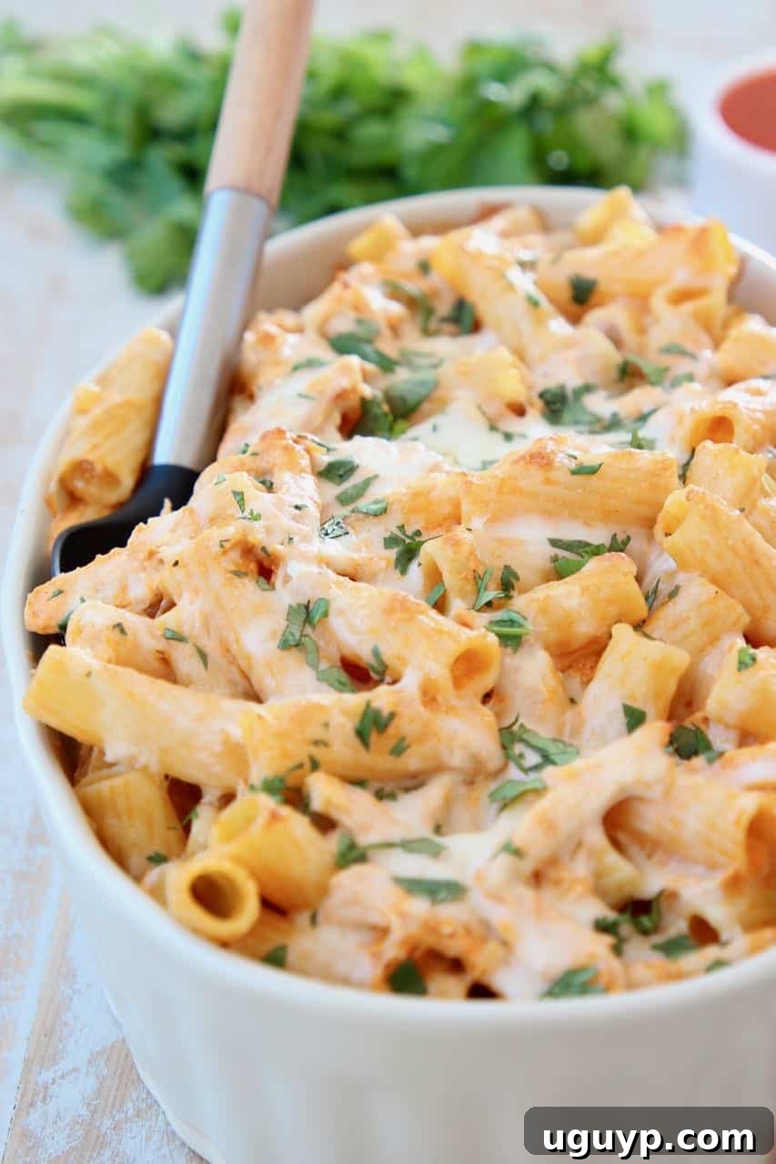 Buffalo chicken baked pasta in a rustic casserole dish, ready to be served, with a serving spoon scooping out a portion, highlighting the melted cheese and pasta. A perfect weeknight dinner or potluck dish.